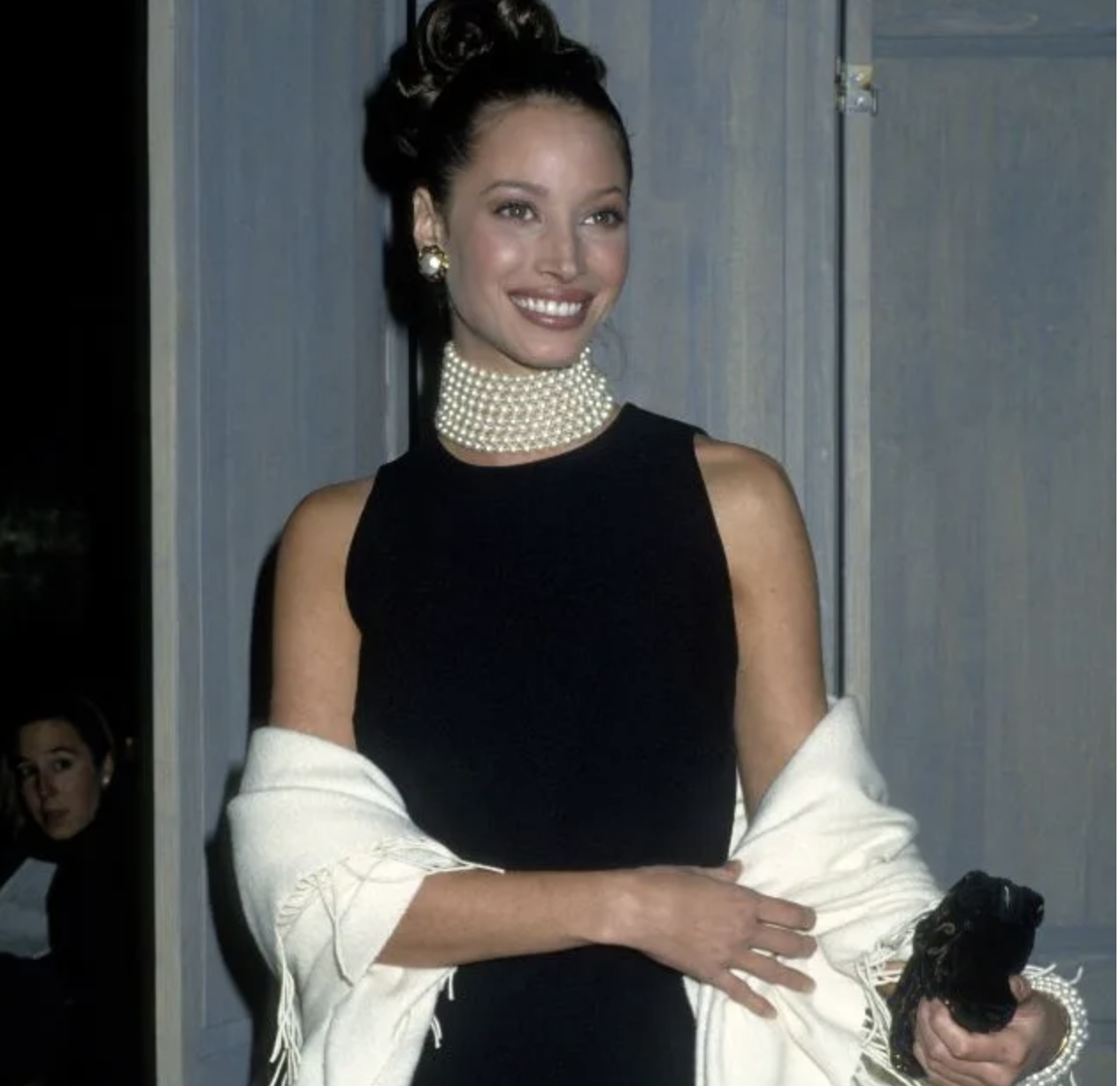 Celebridad en vestido elegante sin mangas con perlas al cuello y chal blanco, sonriendo