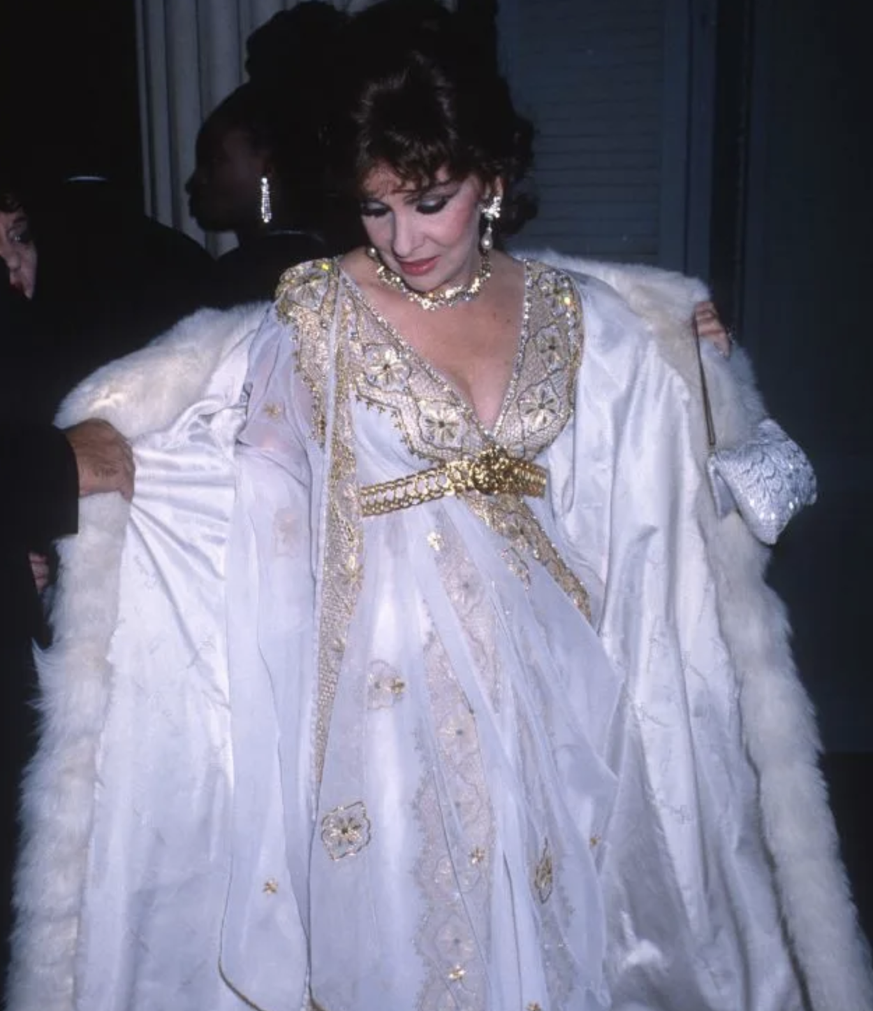 Elizabeth Taylor con vestido blanco adornado y abrigo de piel, estilo glamuroso