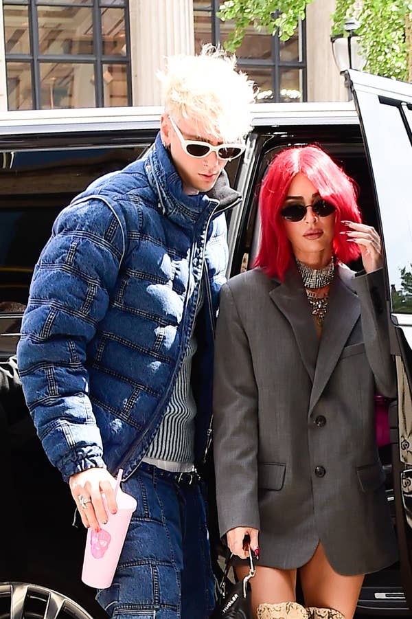Man in a denim jacket and woman with red hair in a grey blazer, exiting a vehicle
