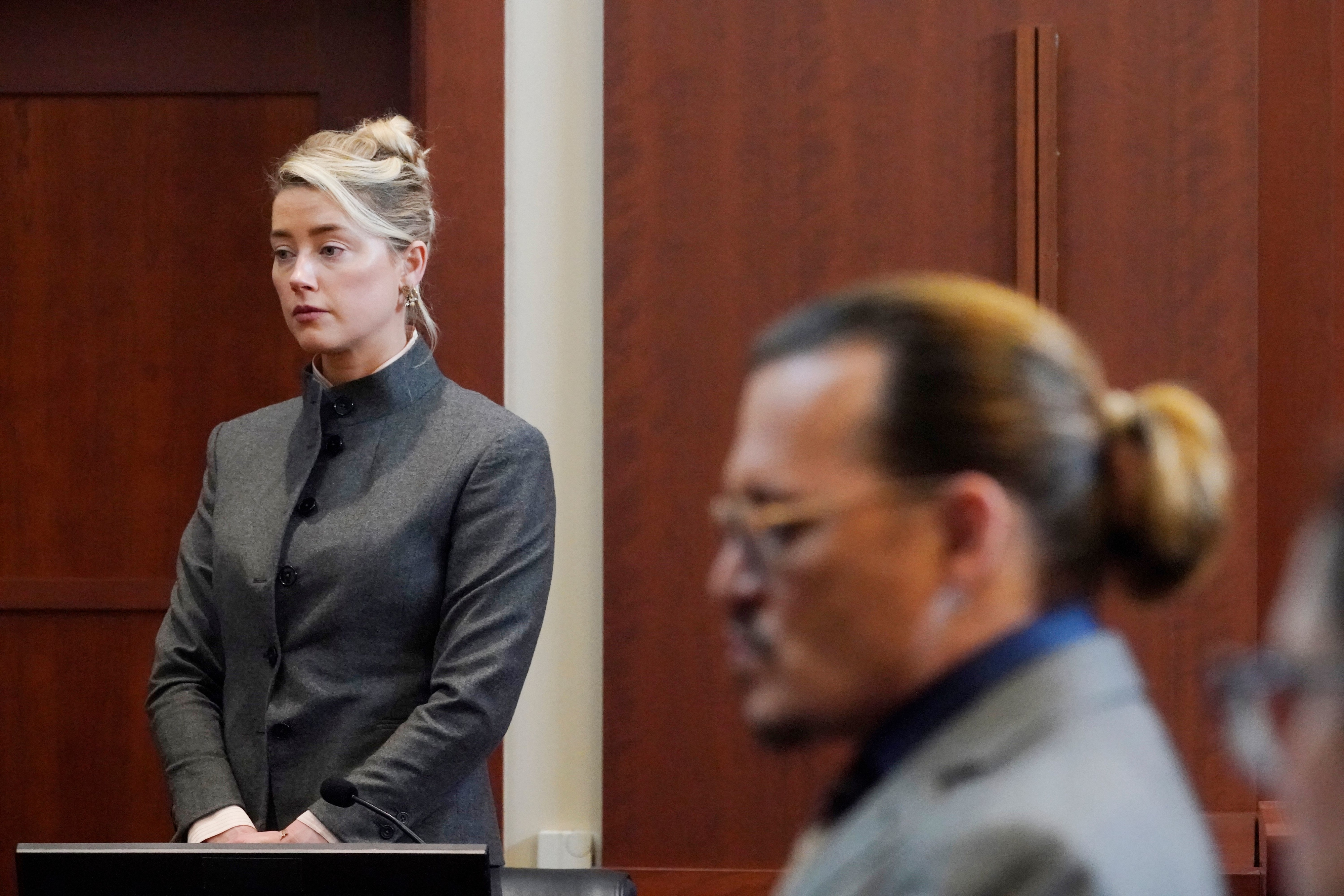 Amber Heard standing in court, wearing a gray suit with her hair up in a bun