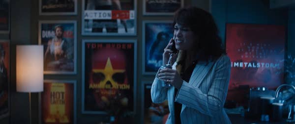 Woman in striped suit holds award, movie posters in background