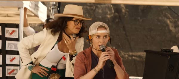 Two women on a film set, one using a microphone, both wearing hats and casual attire