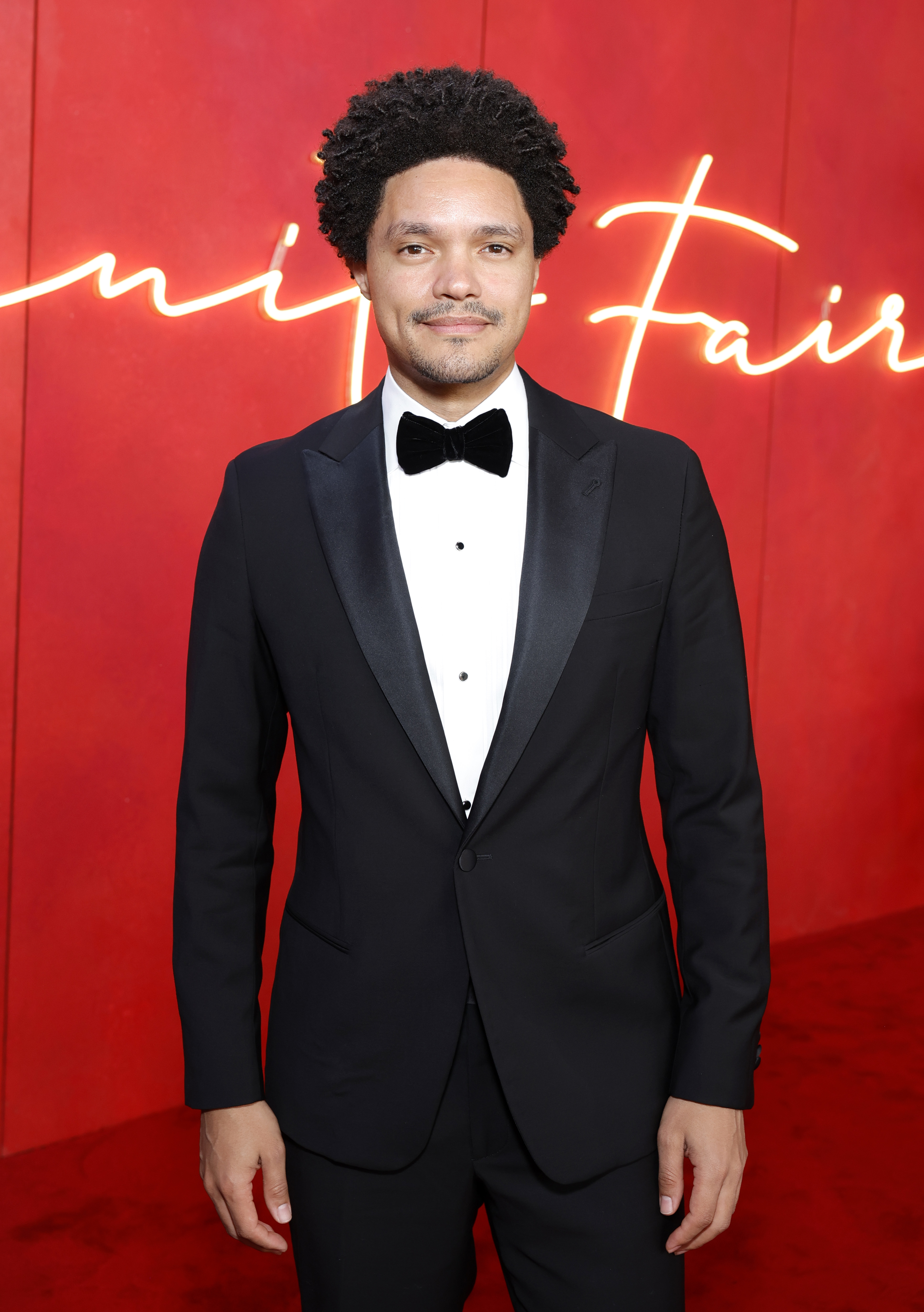 Trevor Noah dressed in a classic black tuxedo with a bowtie at the Vanity Fair event