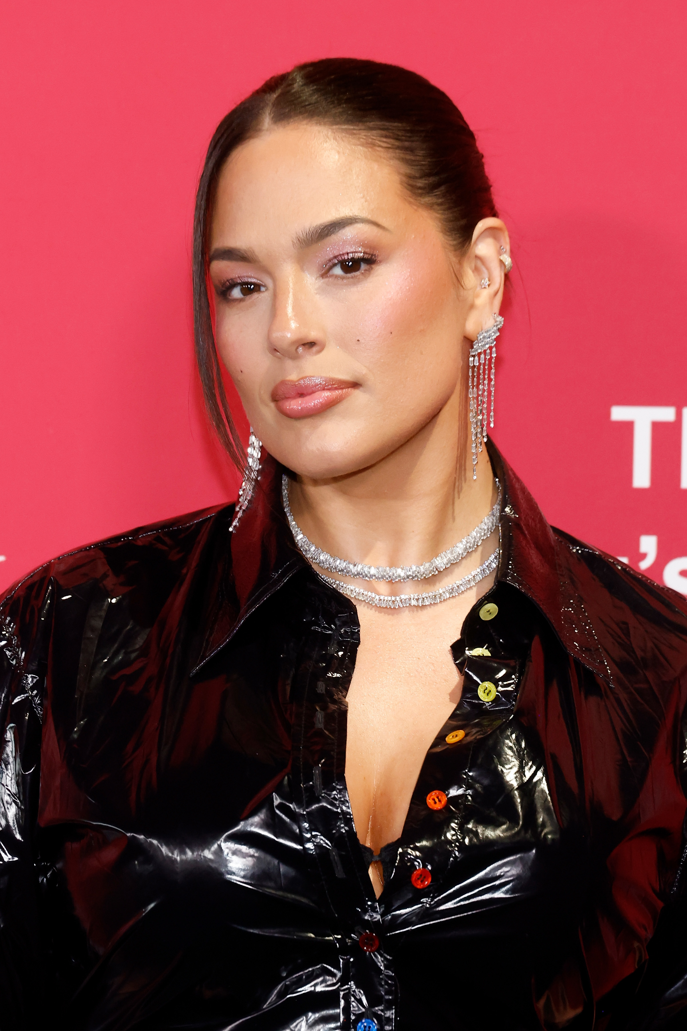 Ashley Graham wearing a glossy jacket and choker with dangling earrings at an event
