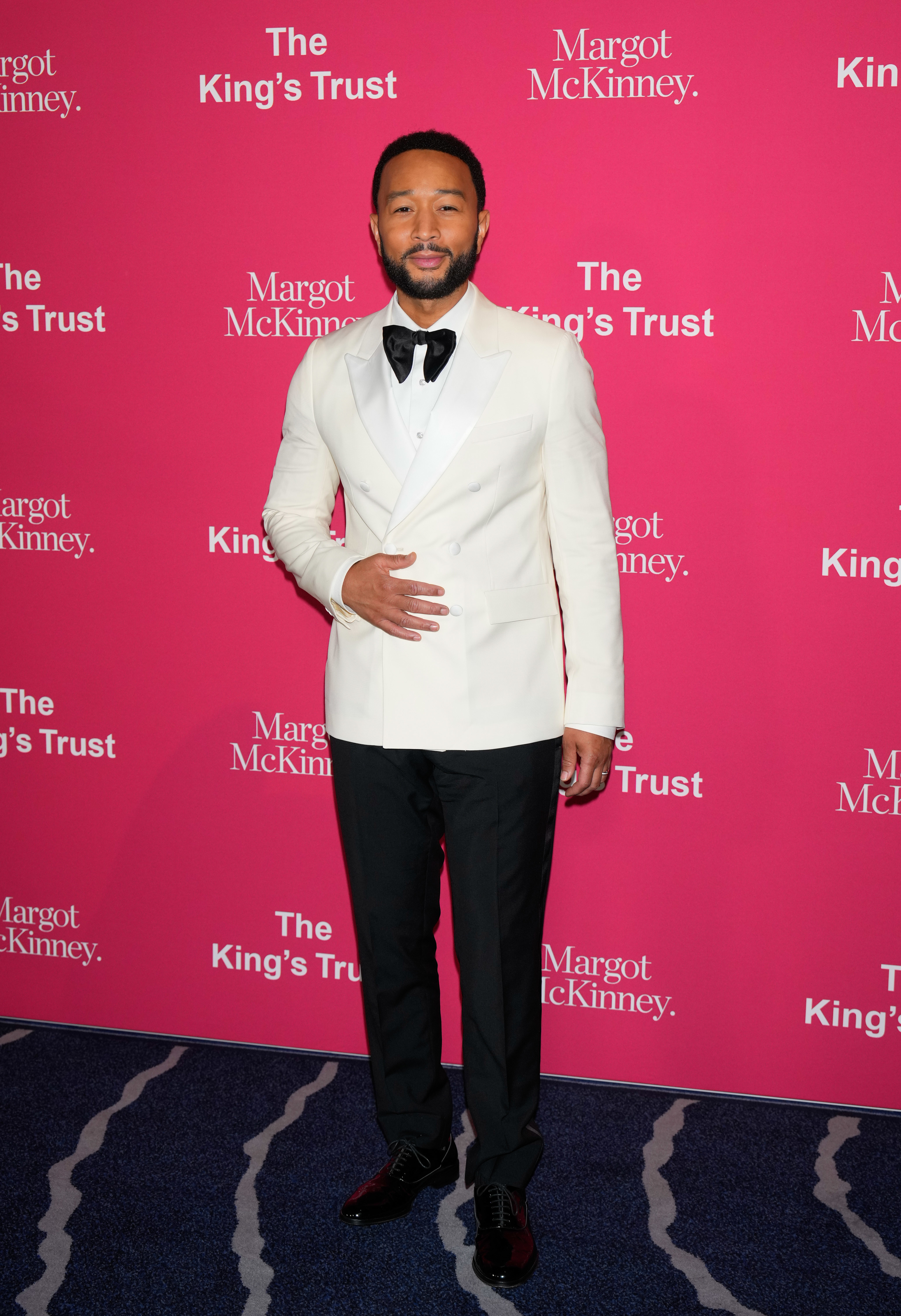 John Legend in a white tuxedo jacket and black bow tie poses at an event