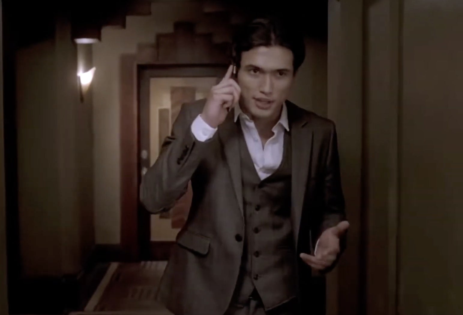 Charles Melton in a suit talking on a phone in a hotel hallway