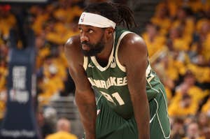 Basketball player in green uniform with 'Milwaukee' emblazoned, leaning forward resting on his knees during a game