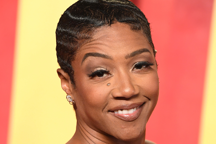 Tiffany Haddish posing with a short wavy hairstyle and a strapless ruffled dress, smiling at an event