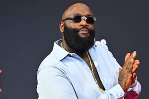 Rick Ross in a light shirt and shades, clapping at an event