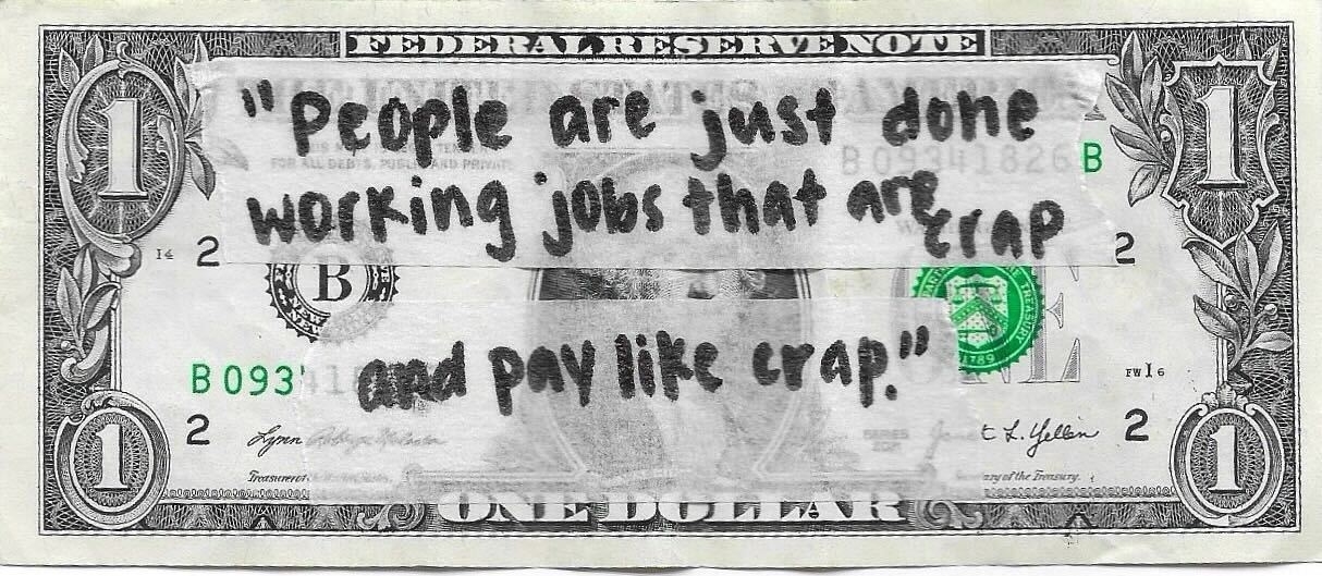 U.S. one-dollar bill with handwritten message about dissatisfaction with job wages