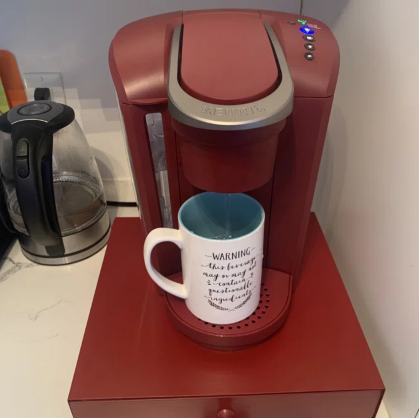 A single-cup coffee maker with a white mug that has a humorous warning about caffeine content