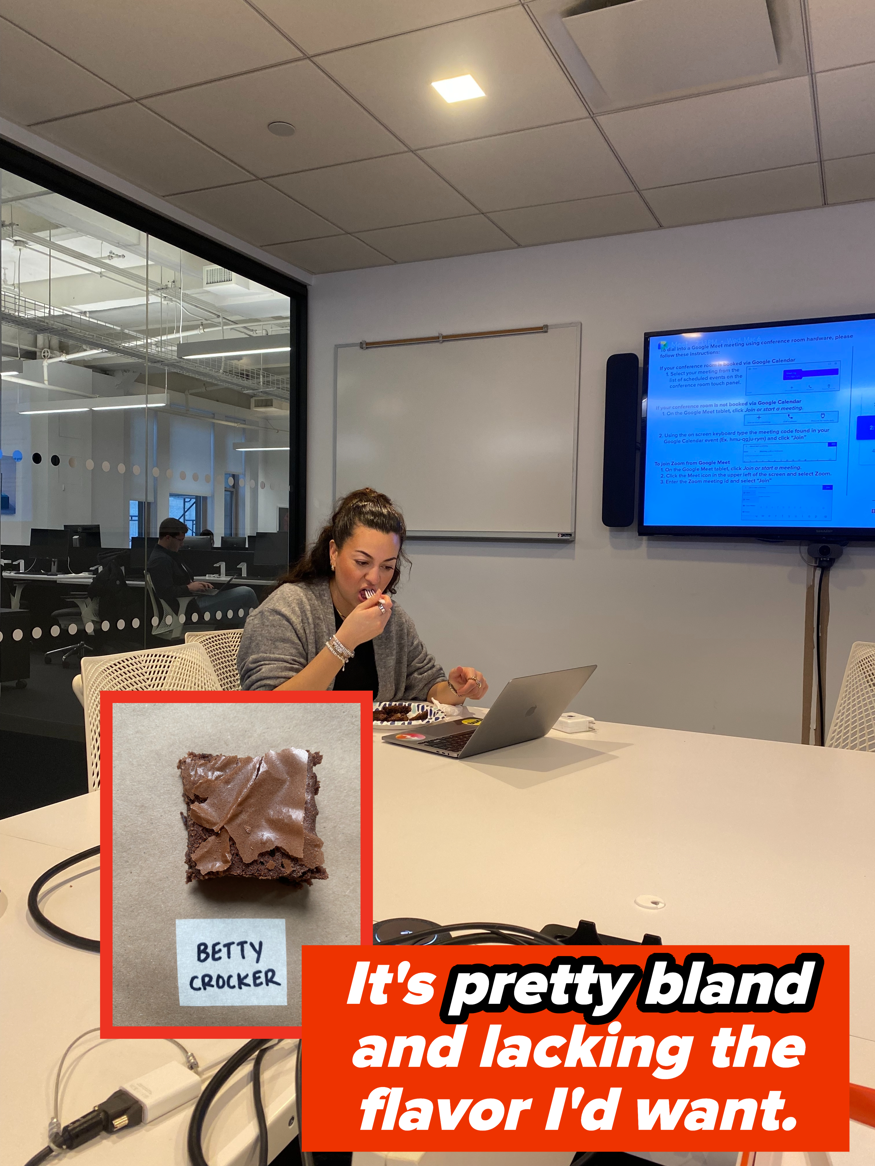 Person at a conference table eating, with a laptop open and presentation screen in the background