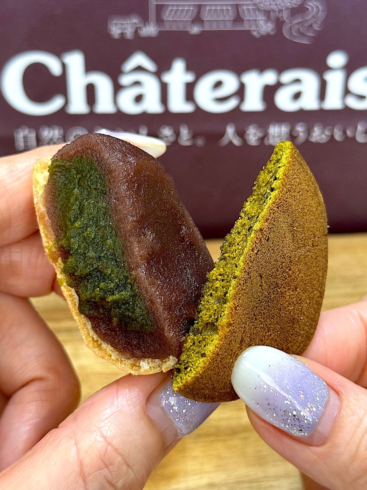Person holding a matcha-flavored dorayaki, a Japanese sweet with green filling, in front of a Châteraisé sign