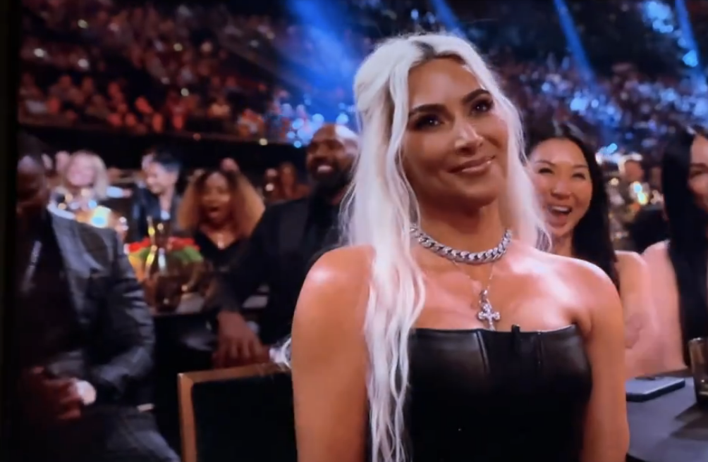 Kim Kardashian in a black dress and chain necklace at an event, smiling and looking to her right