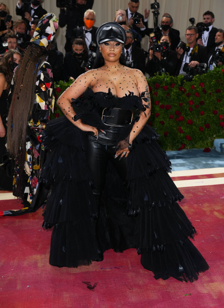 Nicki stands on red carpet, wearing a dramatic ruffled outfit with a headpiece