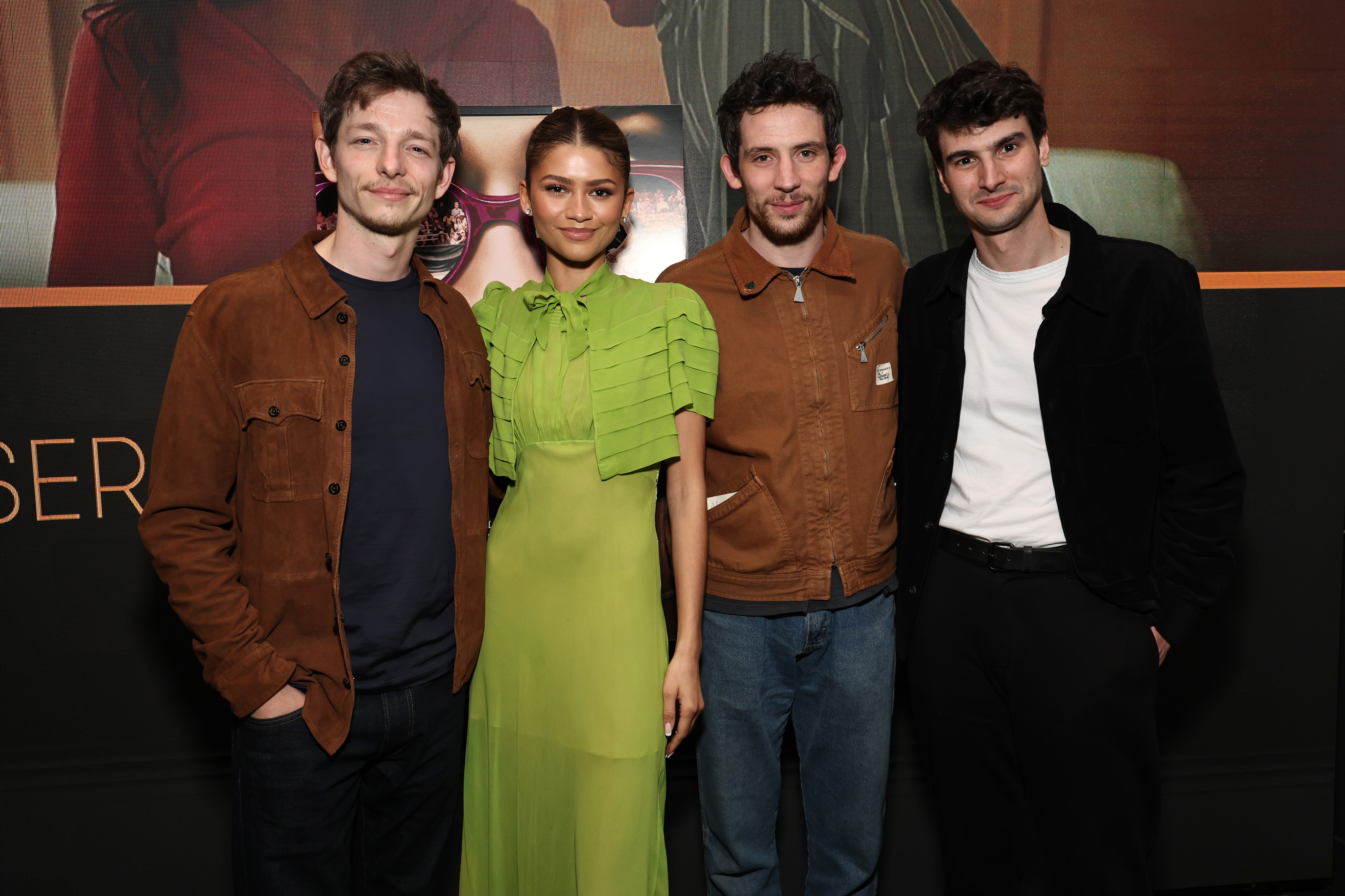 Four celebrities posing; one in a green pleated dress and three in casual attire