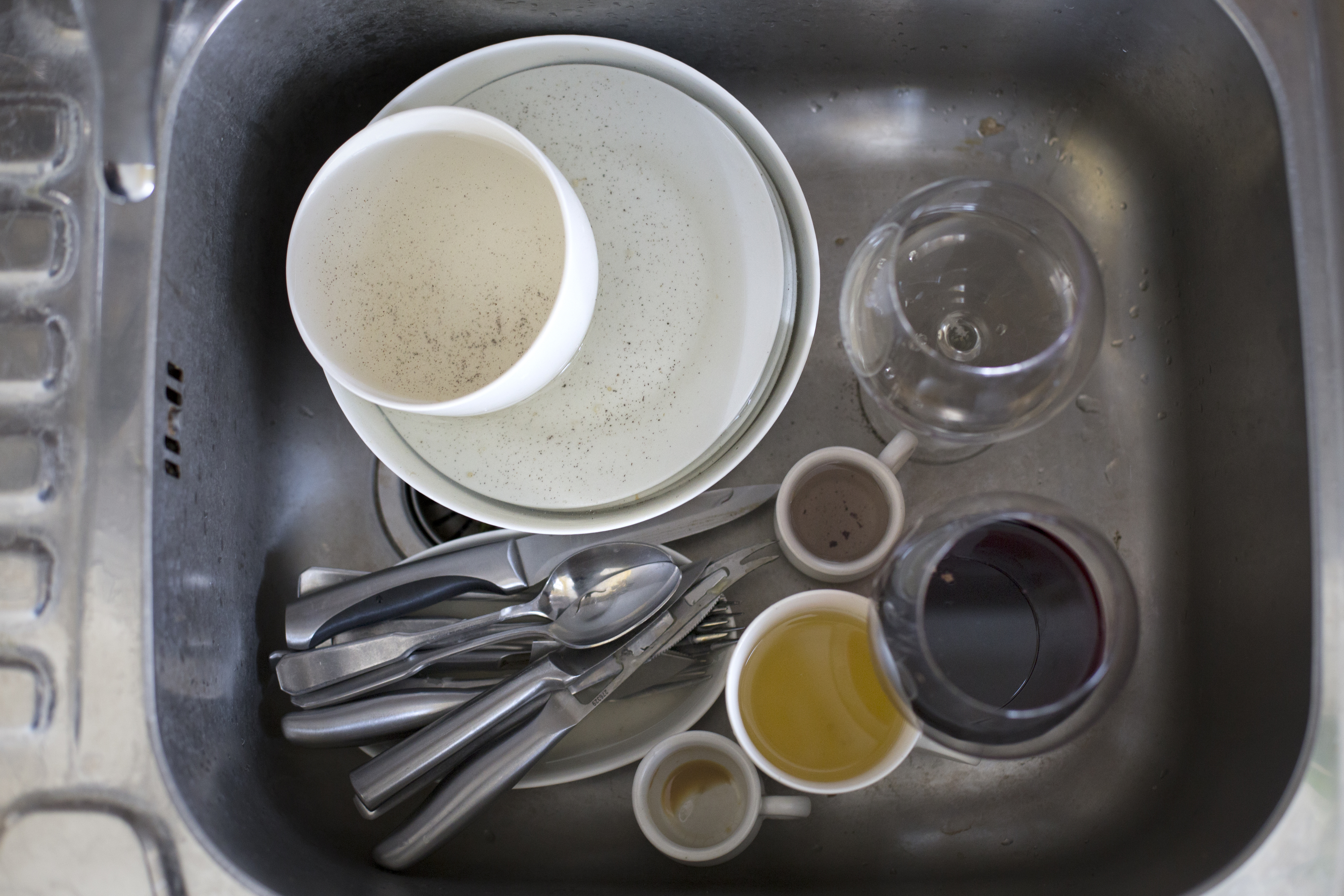 A kitchen sink filled with various dirty dishes including plates, cups, and utensils