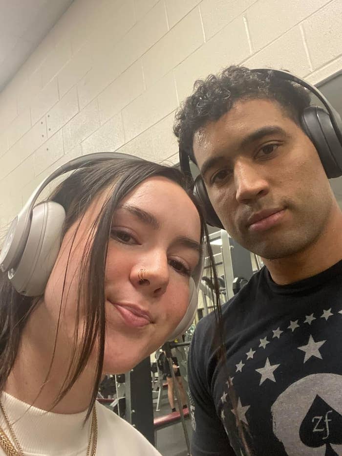 Two reviewers wearing the headphones take a selfie in a gym setting