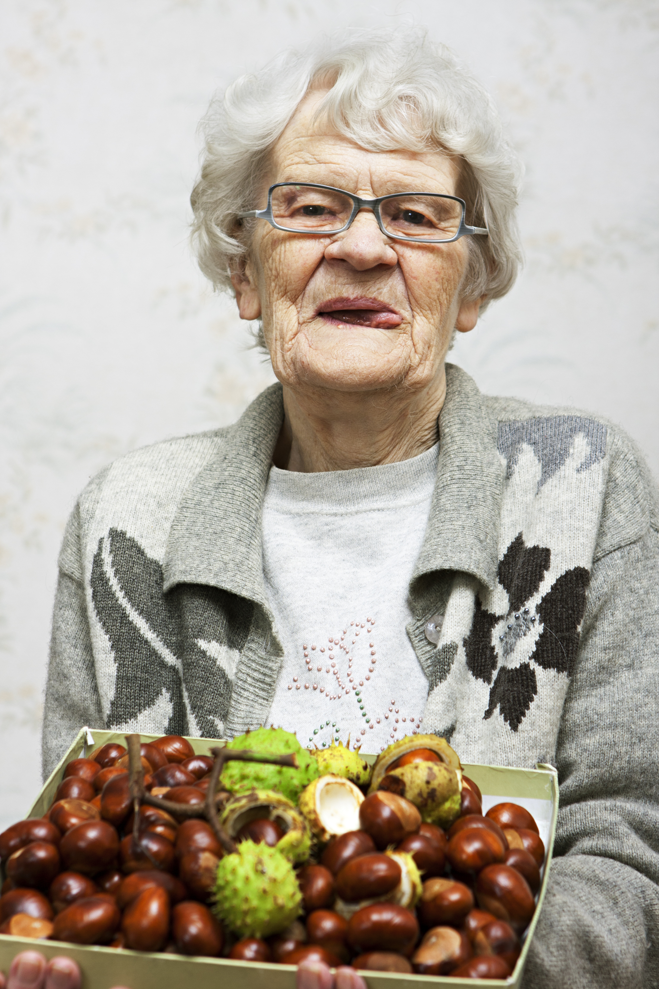 Elderly woman smiling, holding a tray of chestnuts