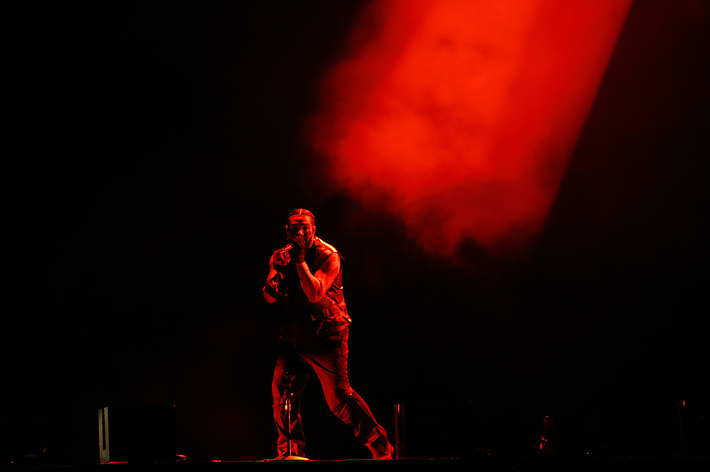 Music artist performing on stage with a microphone under dramatic red lighting