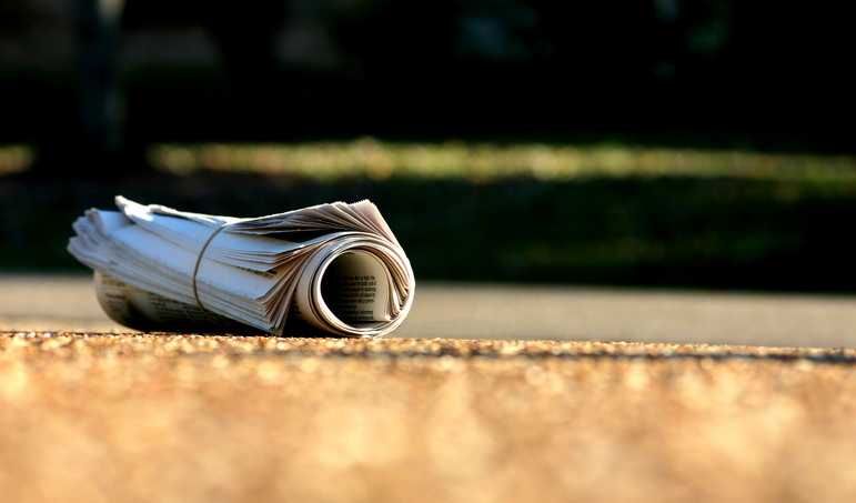 Rolled-up newspaper on a driveway, symbolizing a family&#x27;s morning routine
