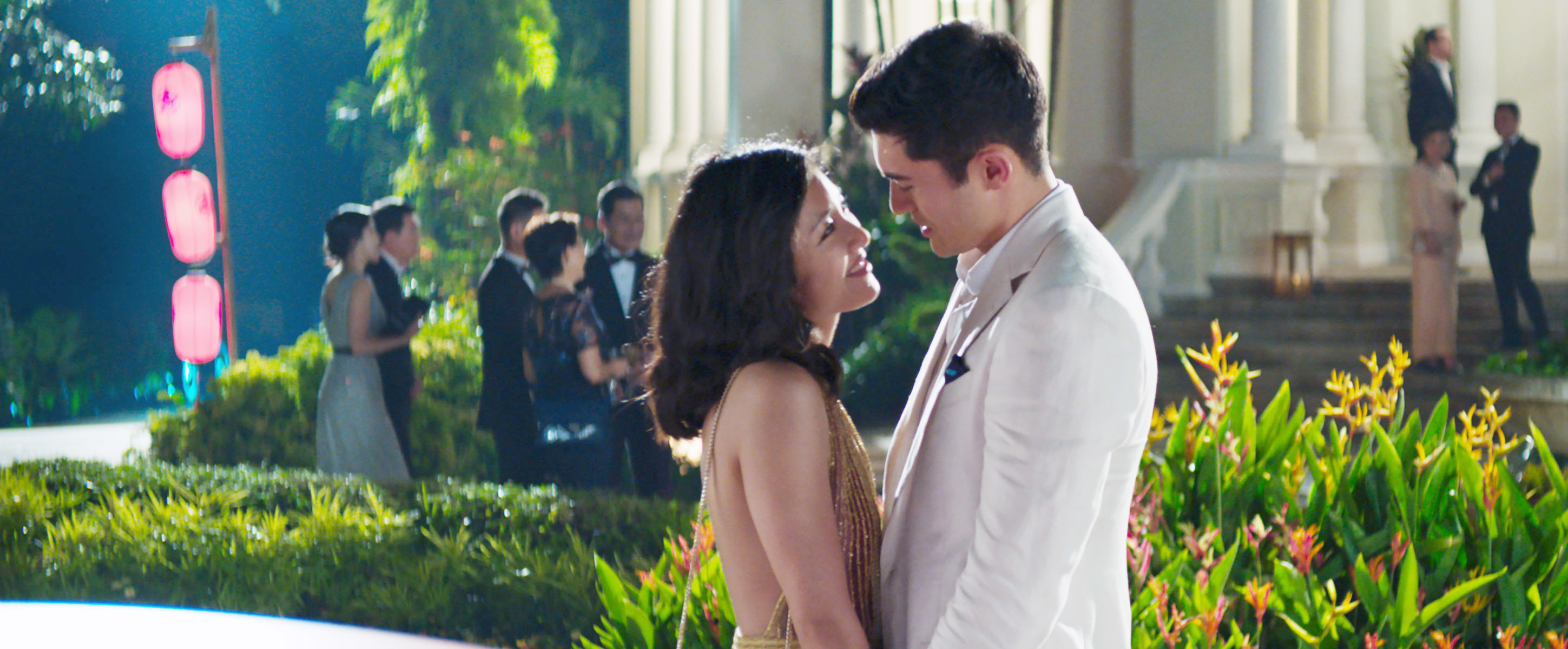 Constance and Henry in a romantic scene, facing each other with a party in the background