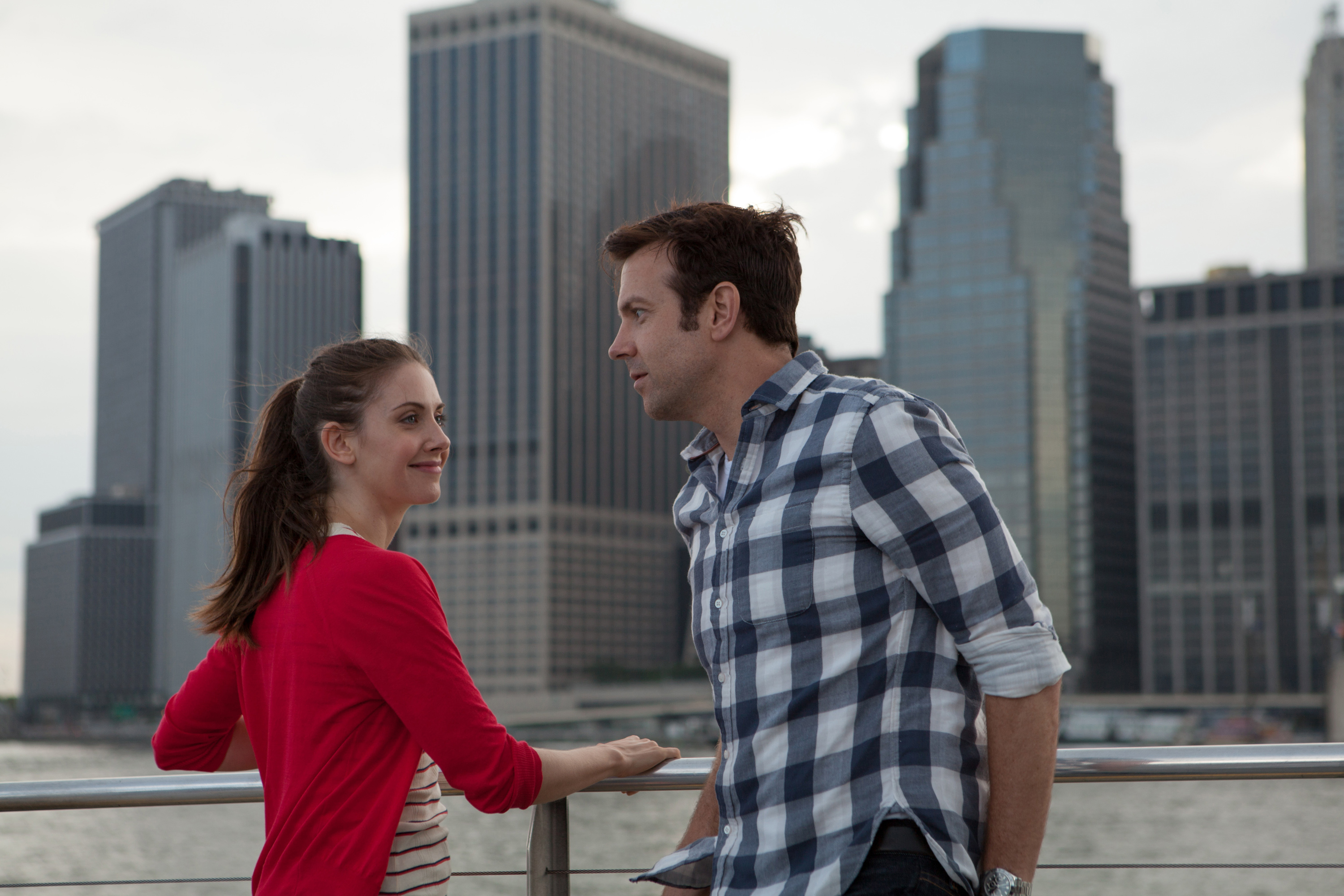 in a scene, Alison and Jason conversing by a railing with city skyline behind, from the movie &quot;Sleeping with Other People&quot;