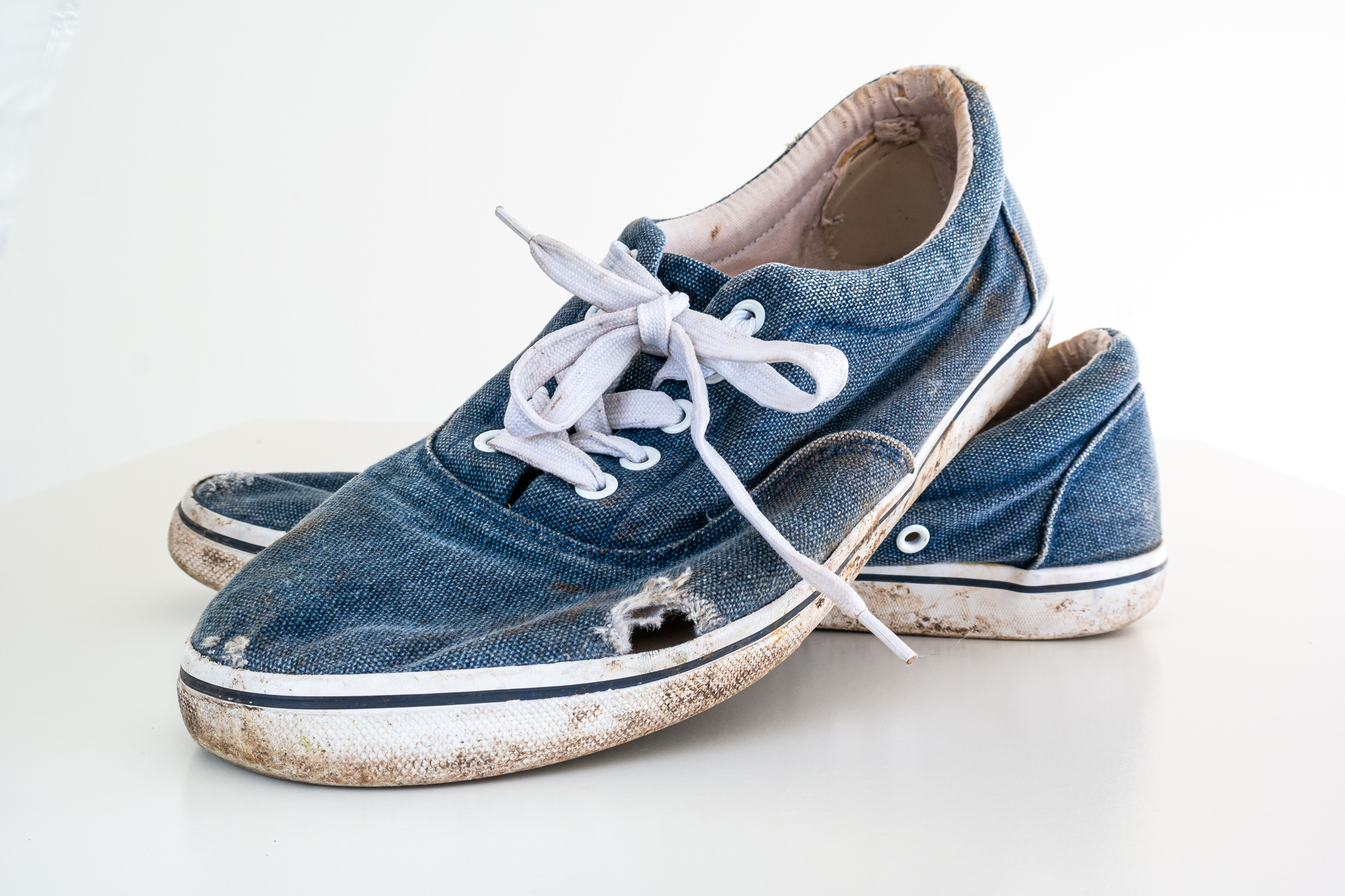 A pair of worn-out kids&#x27; sneakers with untied laces