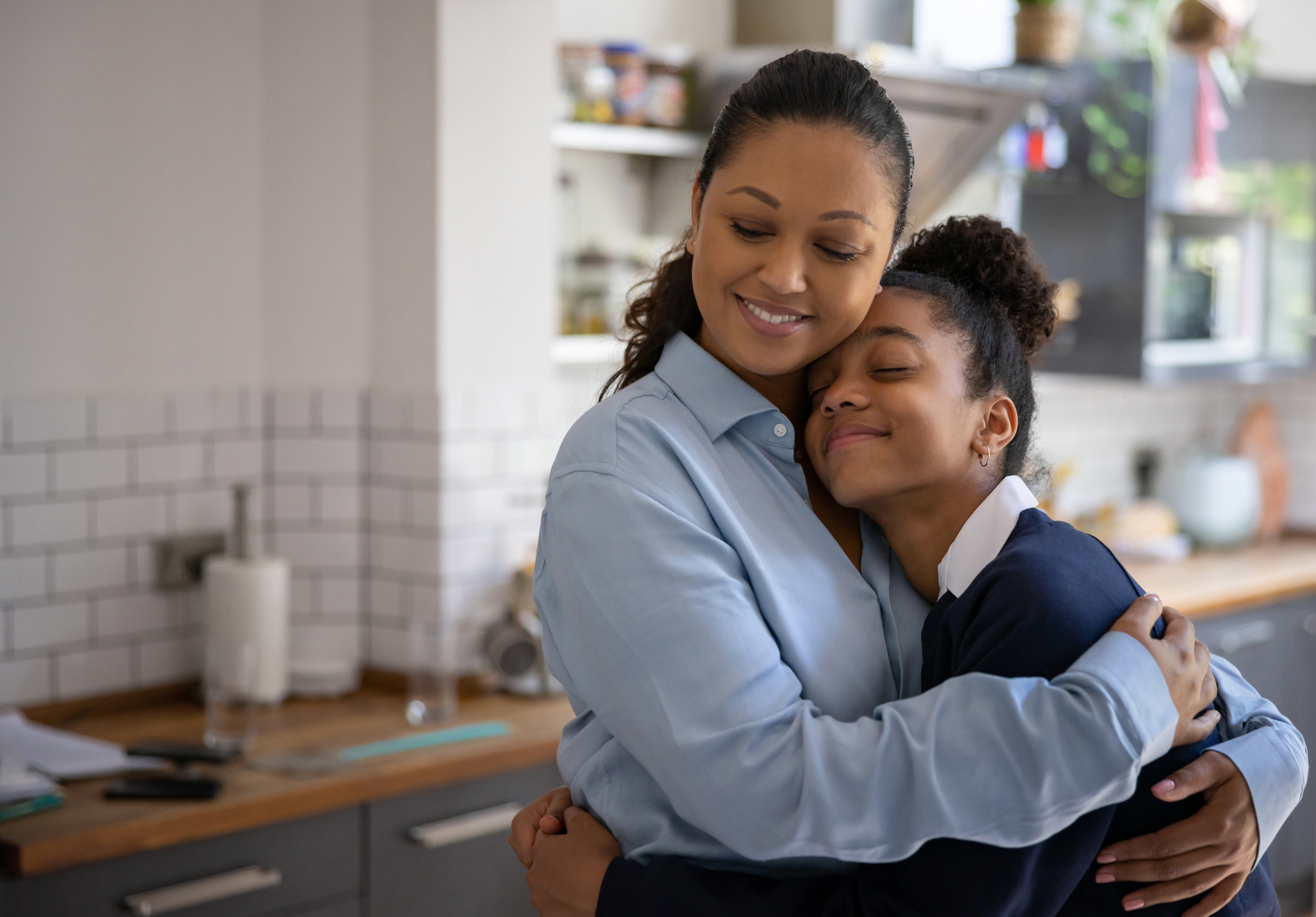 Woman embracing child in kitchen, both smiling, conveying a warm, nurturing moment