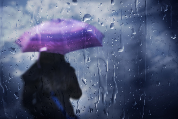 Silhouette of a person under a purple umbrella seen through a rain-streaked window