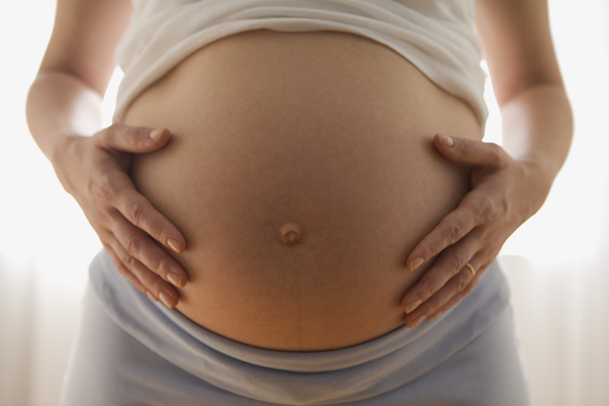 Pregnant person cradling their belly, focus on the midsection. Article context: parenting