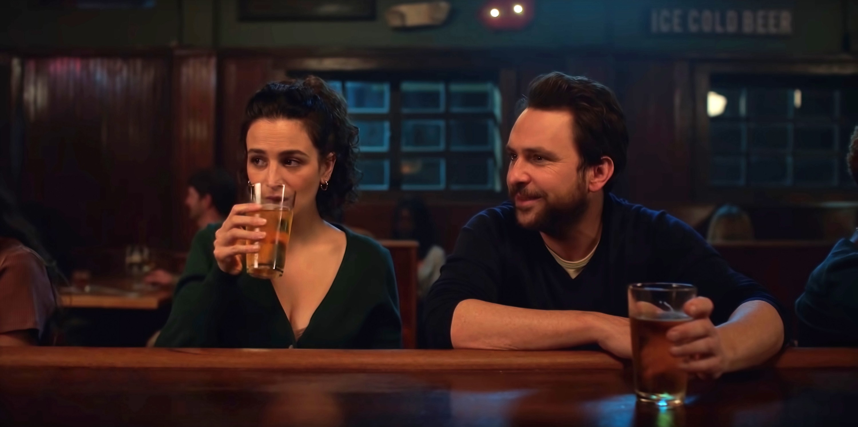 Jenny and Charlie seated at a bar, having drinks, in a scene