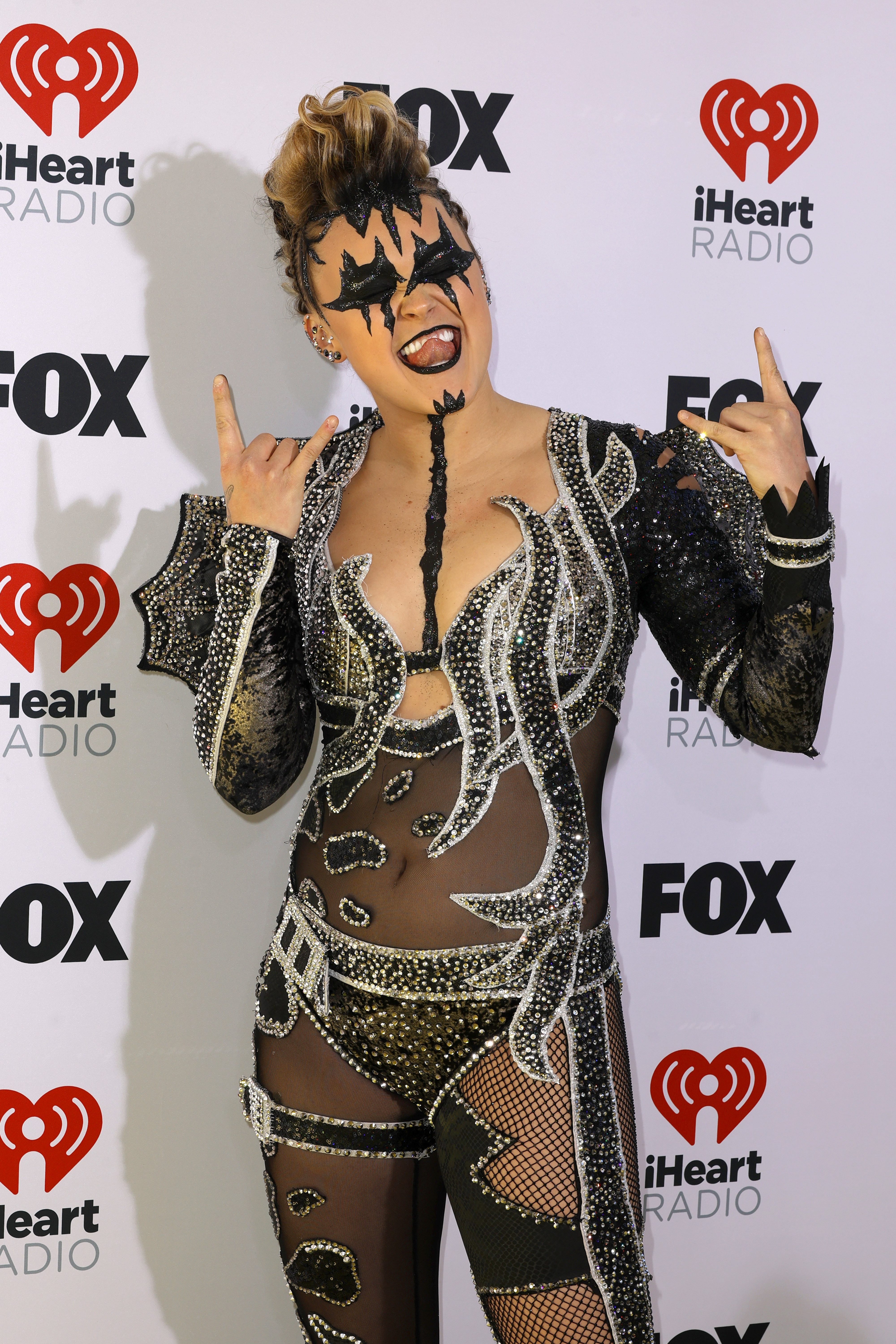 JoJo Siwa in a black embellished jumpsuit with cutouts, making a rock hand gesture
