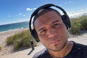 A man wearing headphones takes a selfie with a beach backdrop