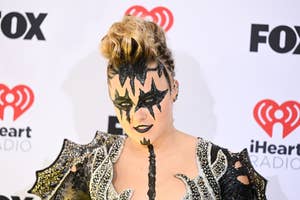 Person with bold face makeup resembling a star, wearing a spiked shoulder outfit
