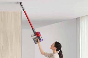 Woman using a cordless vacuum cleaner to reach high cabinet