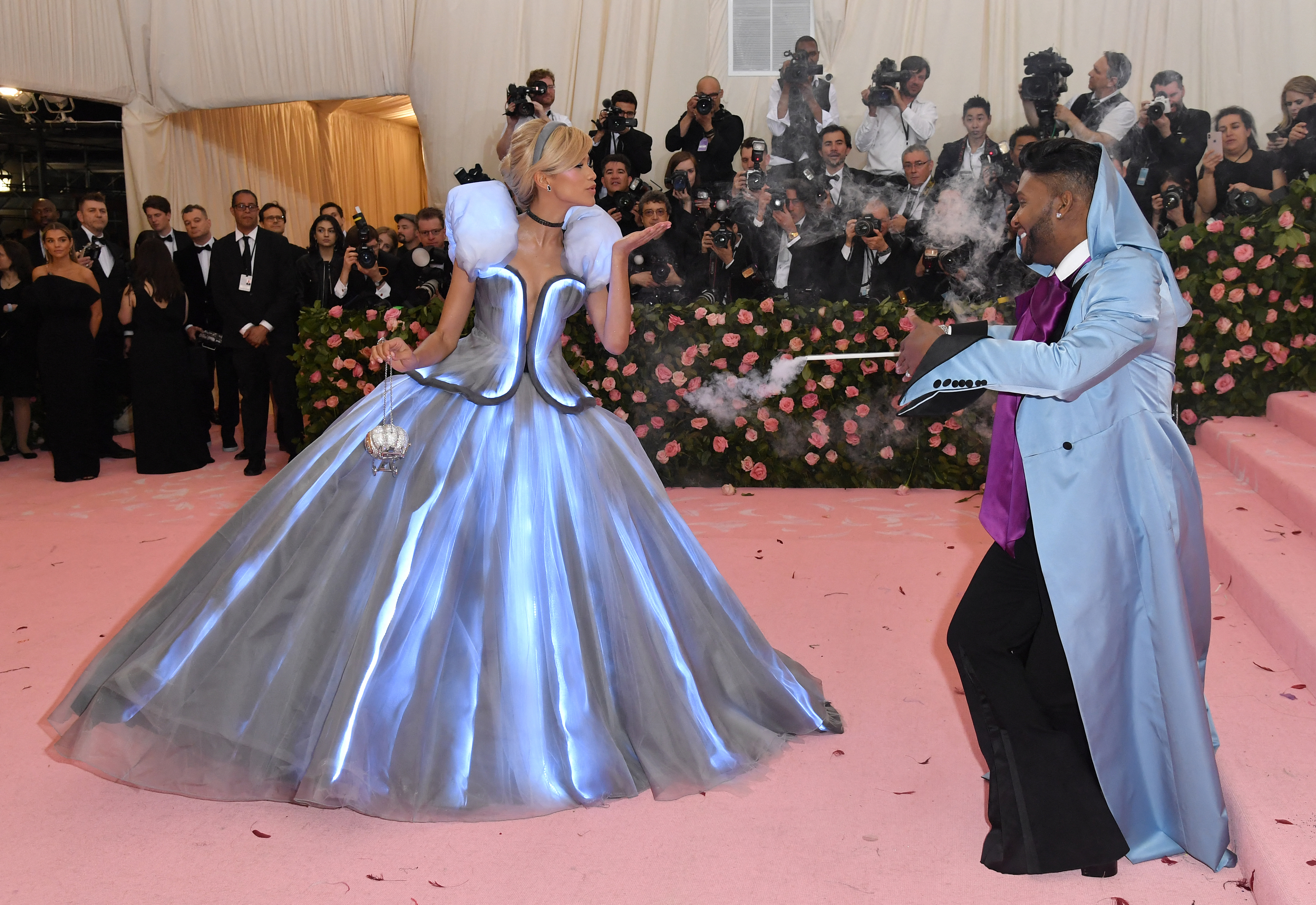 Zendaya in a silver gown with light-up feature and stylist Law Roach in a blue suit at a fashion event
