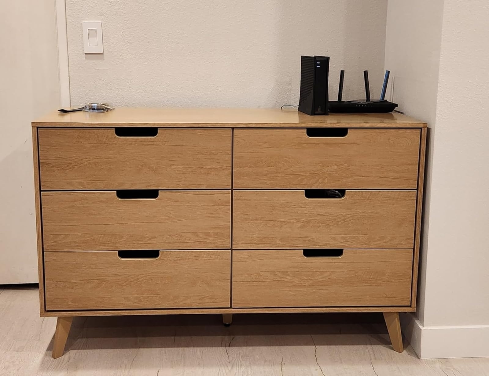 A modern wooden dresser with six drawers, a router and modem on top in a simple room