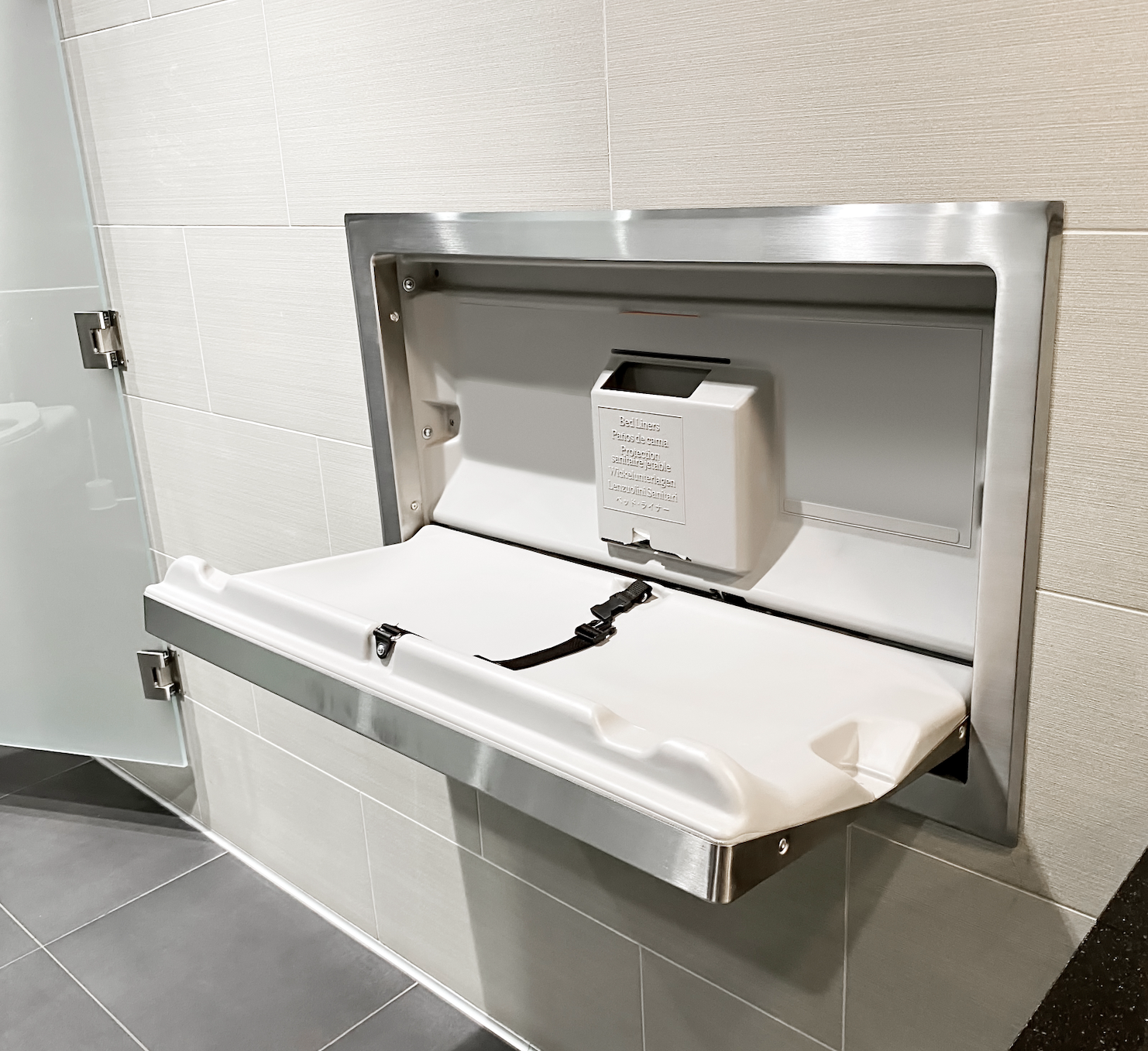 Wall-mounted baby changing station open in a public restroom