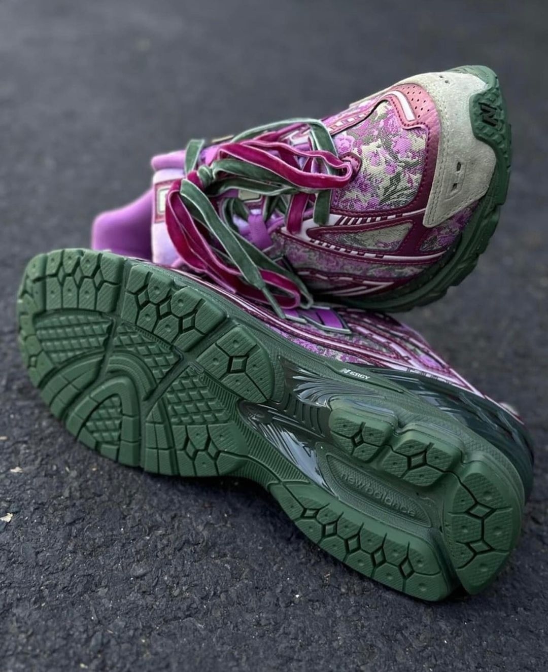 A pair of intricately patterned purple and green sneakers with visible soles, resting on pavement