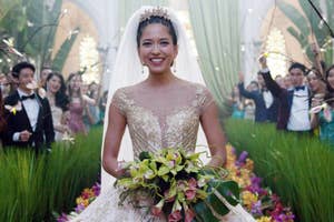 Sonoya MIzuno in beaded gown with bouquet, smiling as guests with sparklers line aisle in celebration as Araminta in Crazy Rich Asians