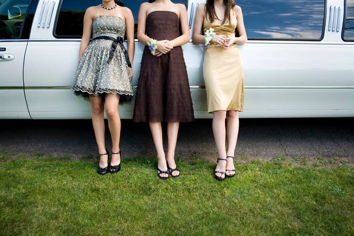 Three women in formal dresses standing in front of a limousine, holding flowers