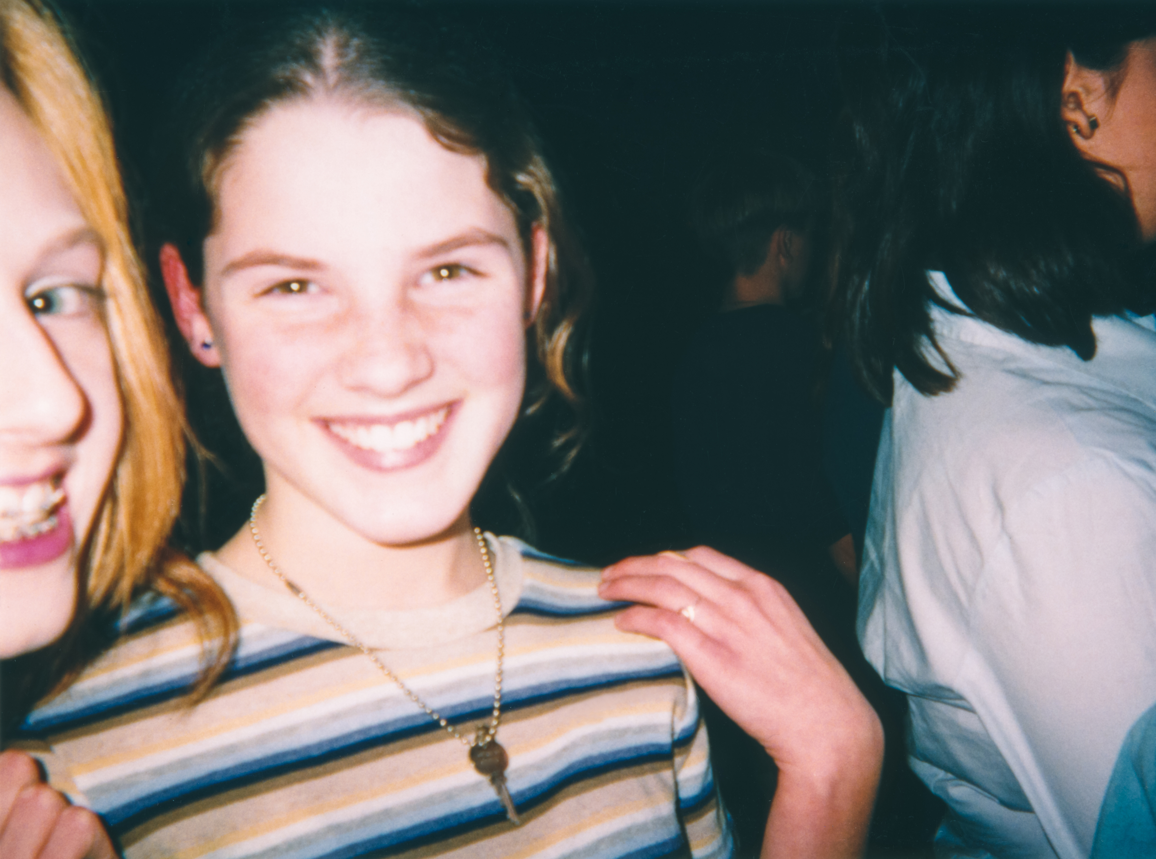 Two individuals smiling for a close-up photo, one partially cropped from left, wearing striped shirt and necklace