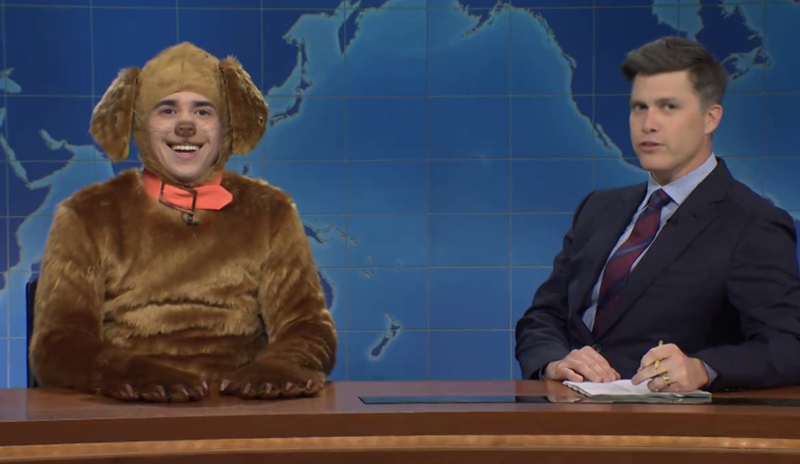 Two performers on SNL; one dressed as a dog with ears and collar, another in a suit at a news desk