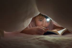 Child reading under blanket with flashlight