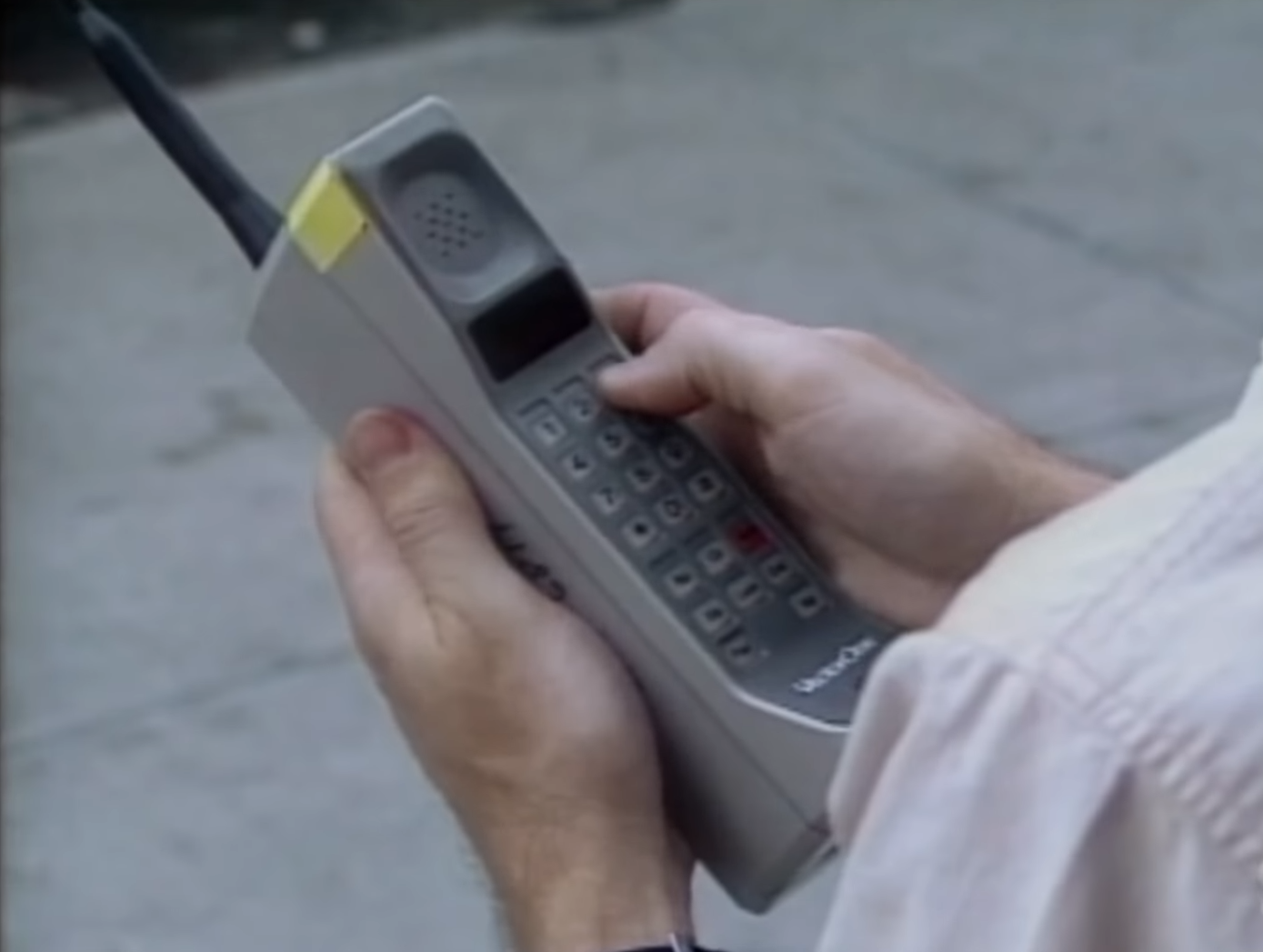 Person holds a large, vintage mobile phone, demonstrating outdated technology in relation to work and connectivity