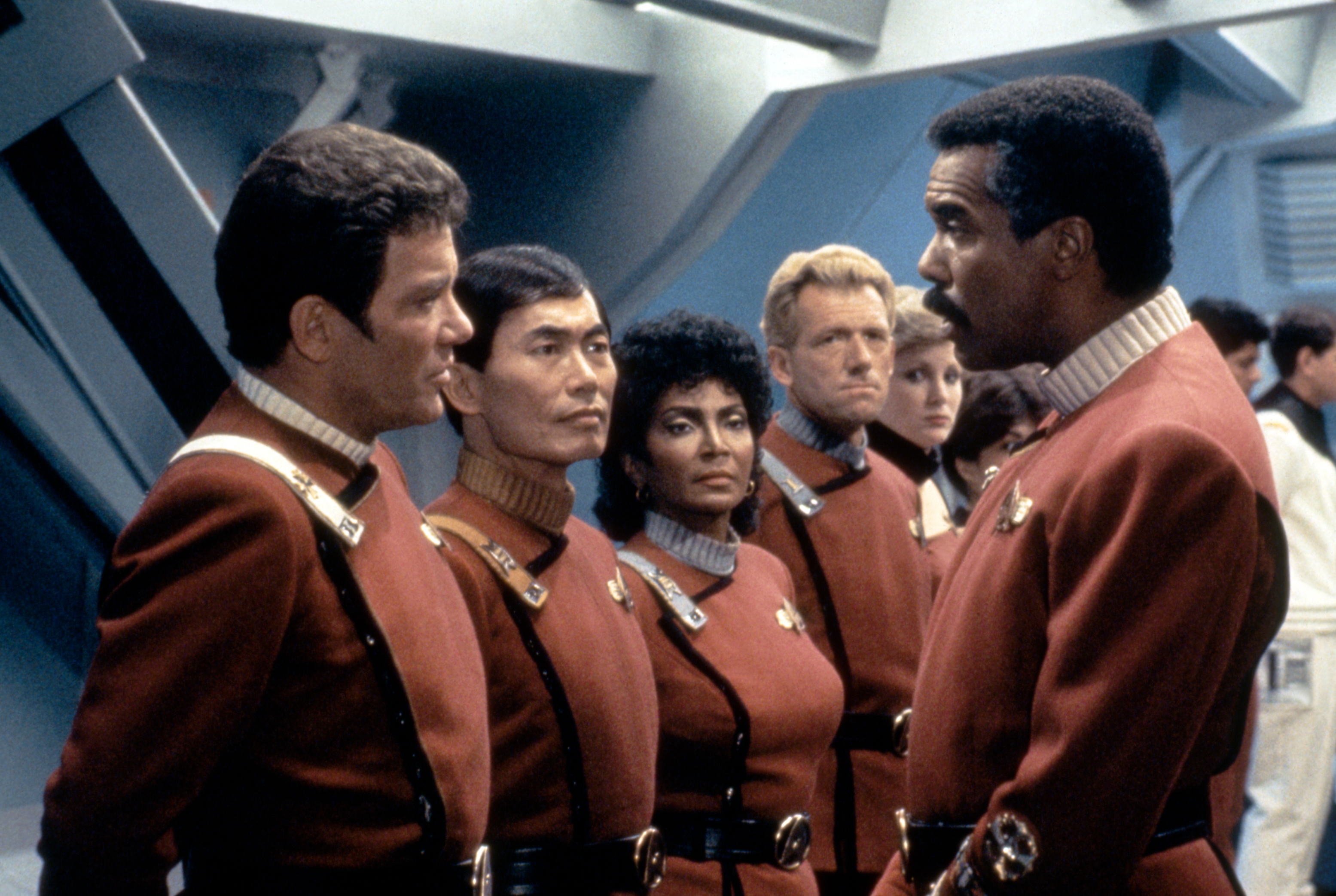 Group of Star Trek characters in uniform, focused on a conversation. Stars include William Shatner and Leonard Nimoy