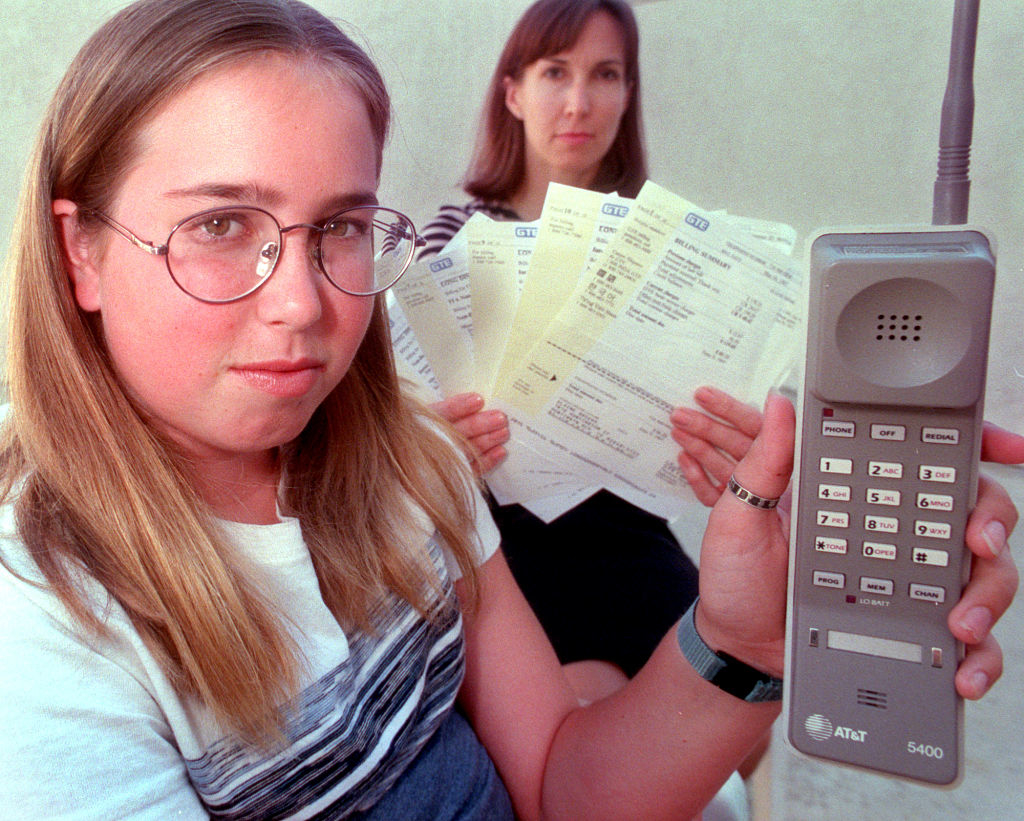 Woman holding multiple bills with a look of concern, displaying a large, outdated mobile phone