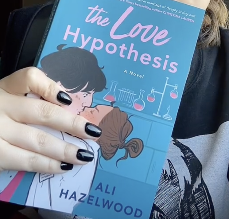 Person holding a book titled &quot;The Love Hypothesis&quot; depicting an animated couple kissing