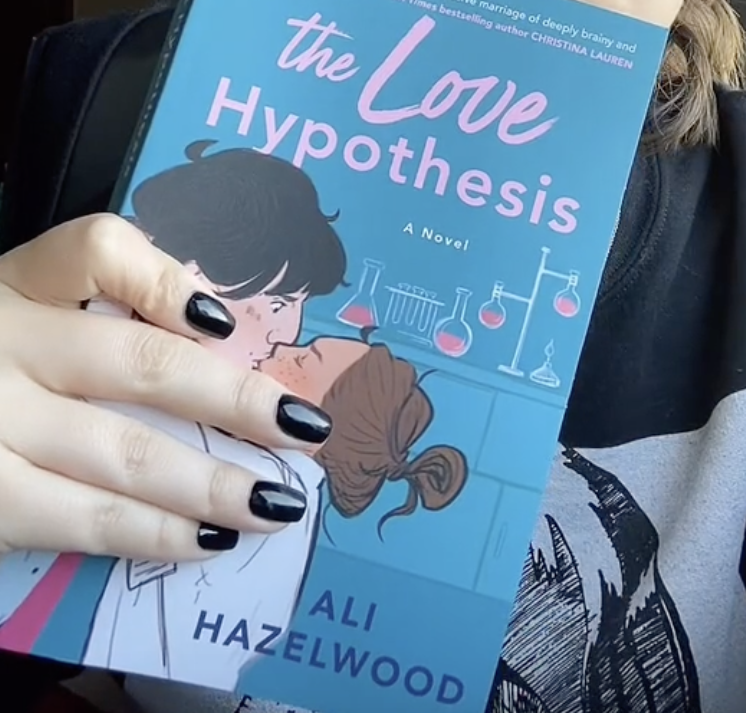 Person holding a book titled "The Love Hypothesis" depicting an animated couple kissing